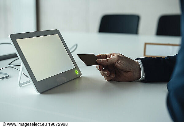 Mature businessman with credit card and tablet PC sitting at desk