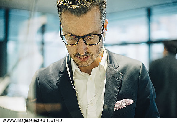 Mature businessman with eyeglasses wearing headphones while looking down in office