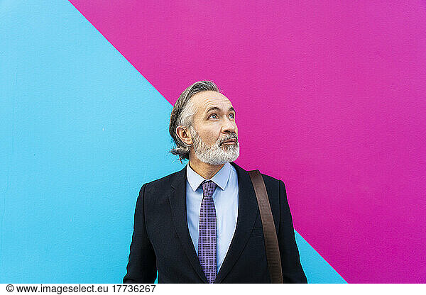Mature businessman with gray hair standing in front of pink and blue wall