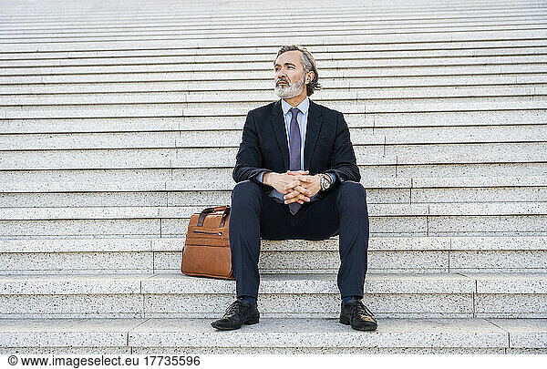 Mature businessman with hands clasped sitting on staircase