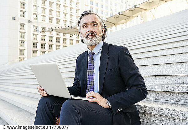 Mature businessman with laptop sitting on staircase