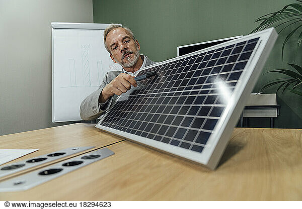 Mature businessman with solar panel sitting at conference table