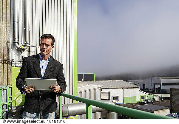 Mature businessman with tablet PC standing at plant