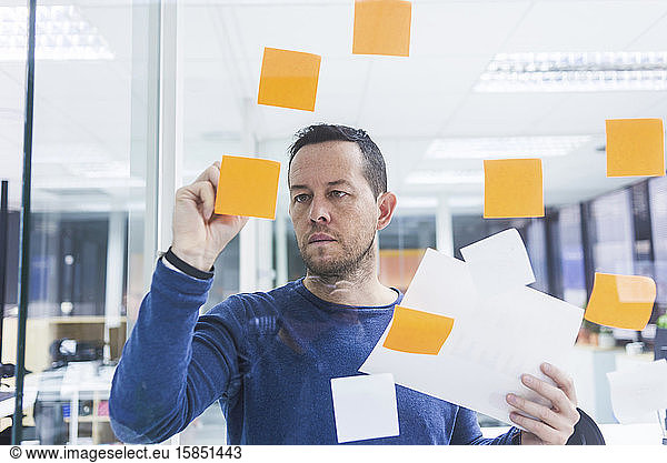 Mature businessman writing on sticky notes at glass pane in office