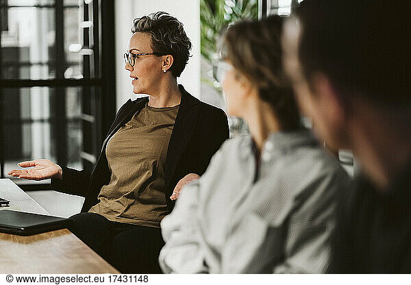 Mature businesswoman brainstorming colleagues while sitting in board room