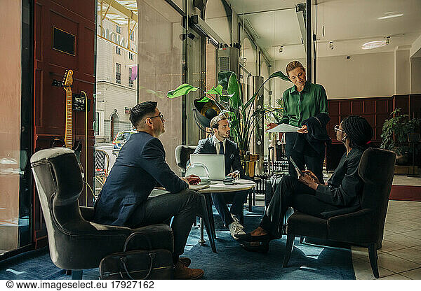 Mature businesswoman discussing ideas with male and female colleagues during meeting in hotel lounge