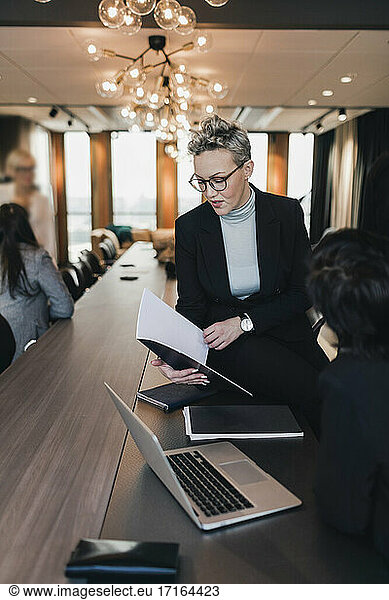 Mature businesswoman discussing over document with female colleague at conference table in board room