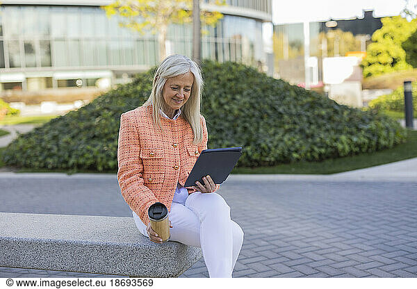 Mature businesswoman doing video call using tablet PC sitting on bench