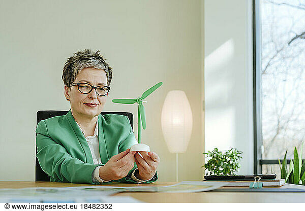 Mature businesswoman looking at wind turbine in office