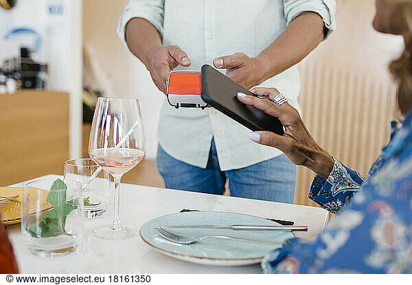 Mature businesswoman making payment through smart phone at restaurant