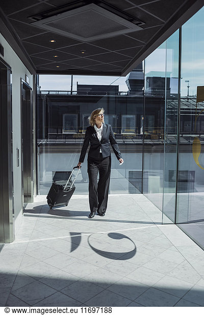 Mature businesswoman pulling wheeled luggage in hotel corridor