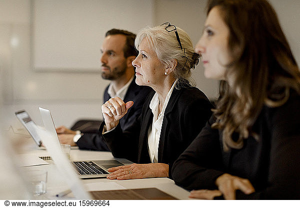 Mature businesswoman sitting with colleagues at conference table in office meeting
