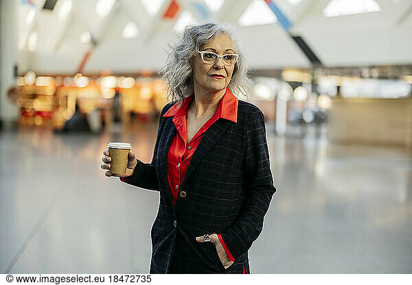 Mature businesswoman standing with disposable coffee cup at subway station