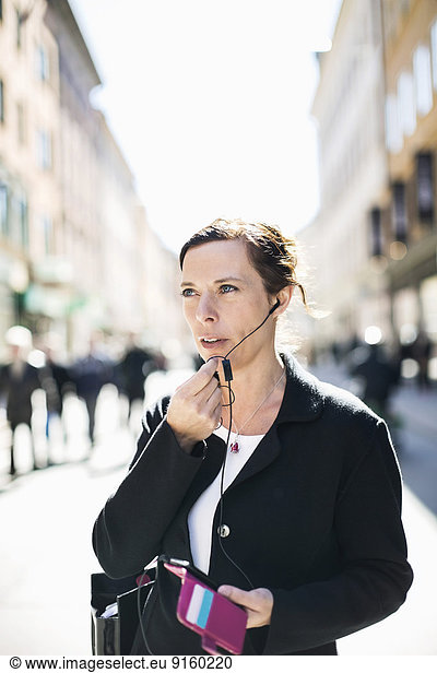 Mature businesswoman talking through headphones on city street