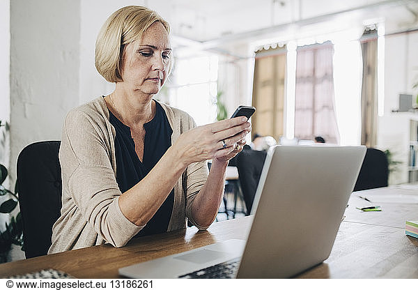 Mature businesswoman using mobile phone at desk in creative office
