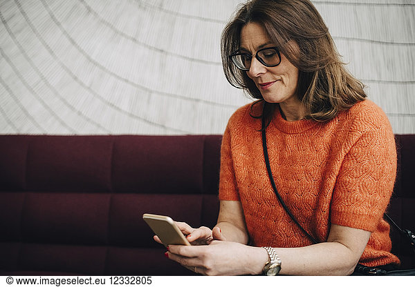 Mature businesswoman using mobile phone while sitting on couch at office