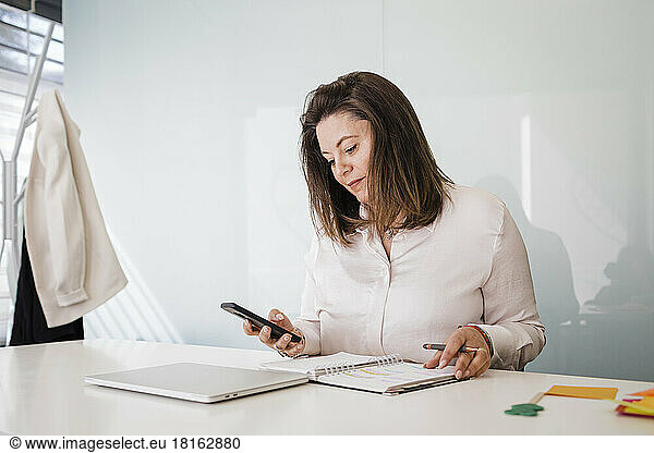 Mature businesswoman using smart phone at desk in office
