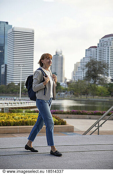 Mature businesswoman wearing backpack walking on footpath