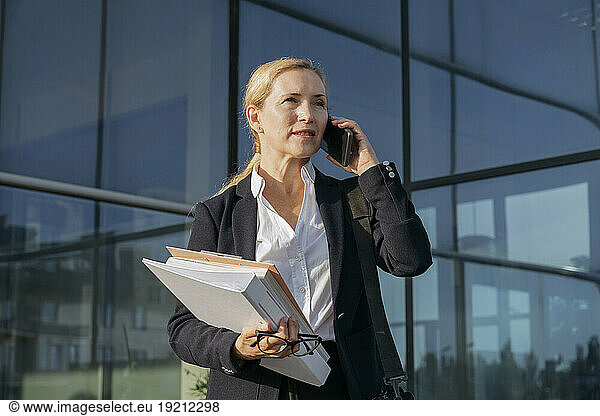 Mature businesswoman with file documents talking on mobile phone