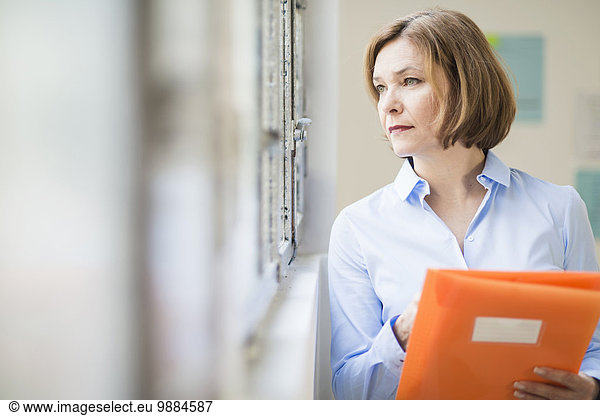 Mature businesswoman with file gazing out of office window