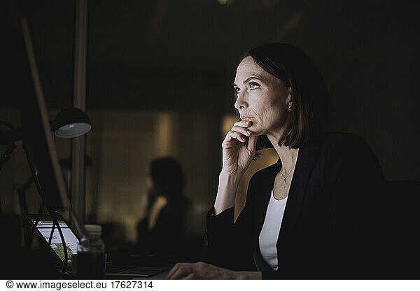 Mature businesswoman with hand on chin working over computer at work place