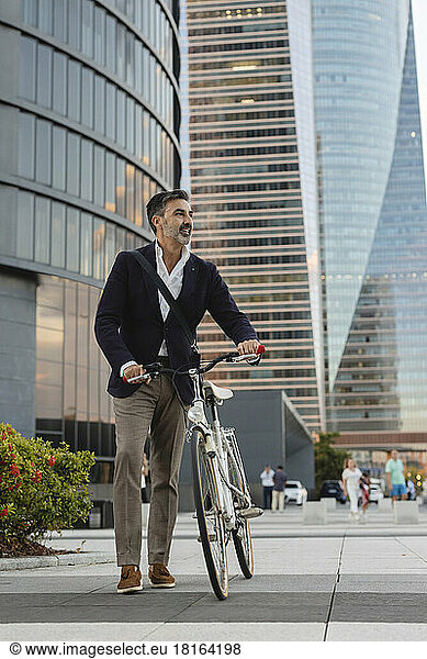 Mature commuter wheeling with bicycle in front of office building