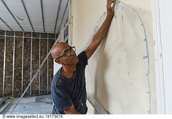 Mature construction worker with mesh sheet on wall at site