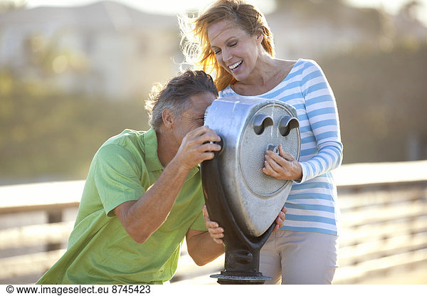 Mature Couple being Playful looking through Scenic Viewer on Pier  USA