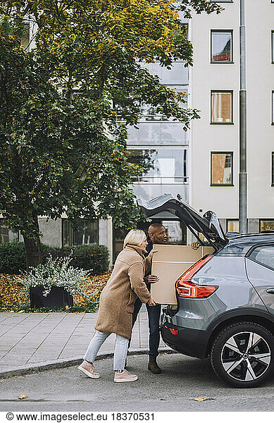 Mature couple loading cardboard together in car trunk during relocation