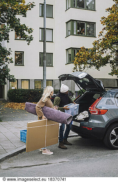 Mature couple loading luggage in car trunk during house relocation