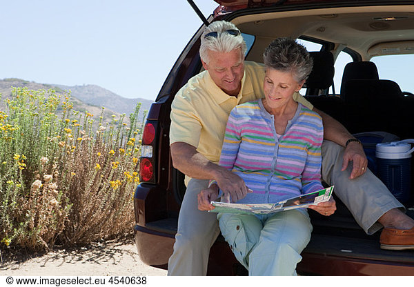 Mature couple sitting on boot of car with map