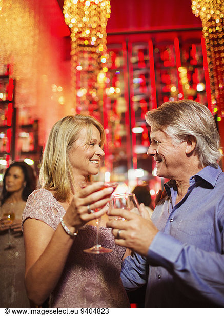 Mature couple standing face to face and holding drinks in nightclub
