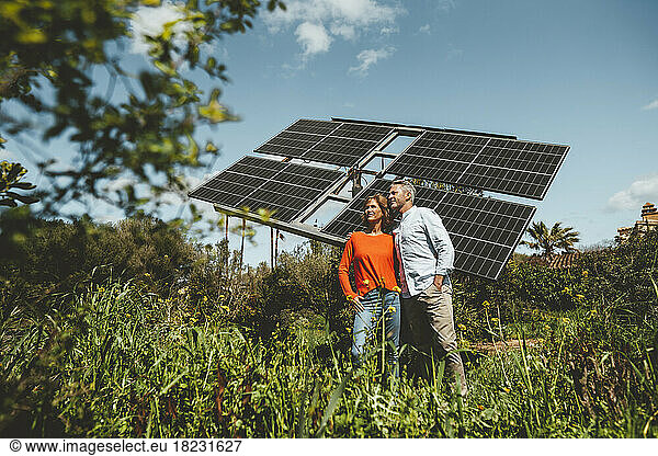 Mature couple standing in front of solar panels at garden