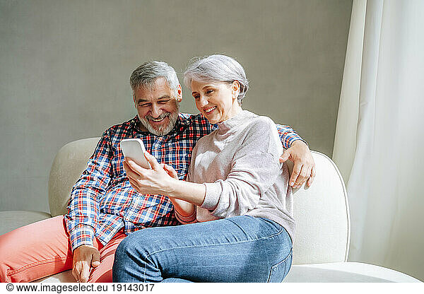 Mature couple using smart phone sitting on couch at home
