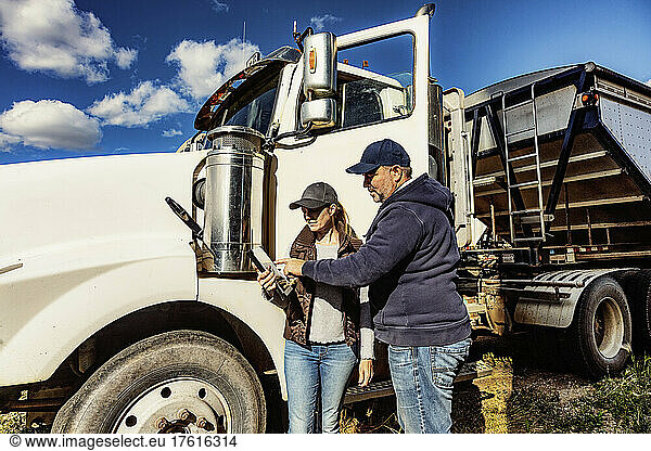 Mature couple working on their farm  standing next to a diesel transport truck and consulting their tablet computer; Alcomdale  Alberta  Canada