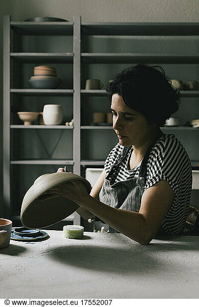 Mature craftswoman painting bowl at table in workshop