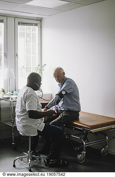 Mature doctor checking blood pressure of senior male patient sitting in clinic