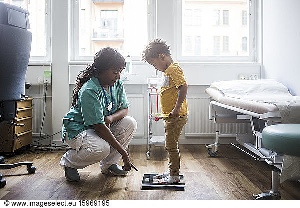 Mature doctor pointing while boy standing on weighing scale in clinic