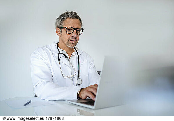 Mature doctor using laptop at desk in medical practice