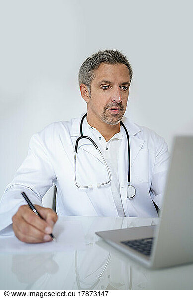 Mature doctor using laptop at desk in medical practice