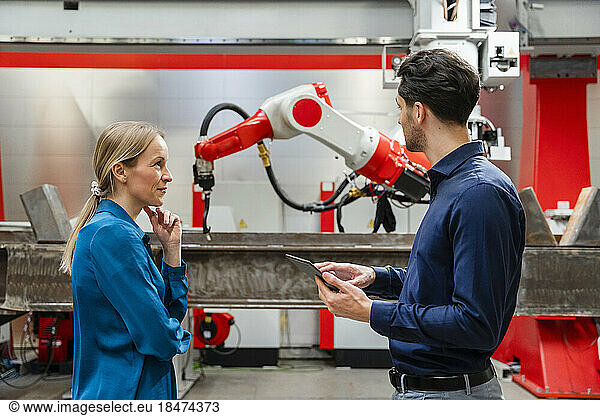 Mature engineer looking at technician holding tablet PC in robot factory