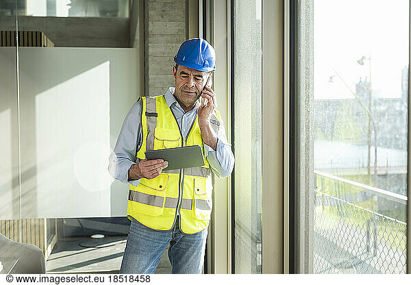 Mature engineer talking on smart phone holding tablet PC in office