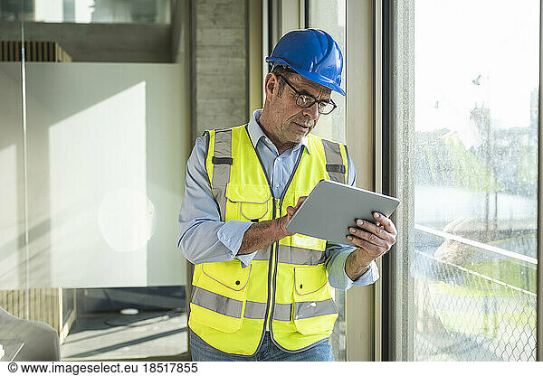 Mature engineer using tablet PC standing by window in office