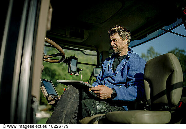 Mature farmer using tablet PC sitting in tractor on sunny day