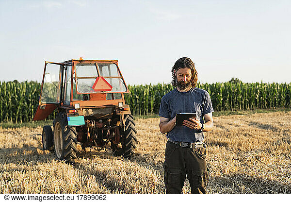 Mature farmer using tablet PC standing in field