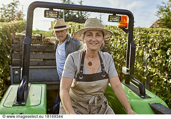 Mature farmers on tractor with crate of grapes in vineyard