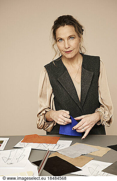 Mature fashion designer holding color sample at desk in studio