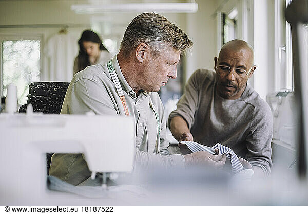Mature fashion designer showing fabric to male colleague at workshop