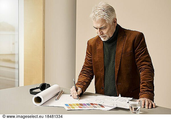 Mature fashion designer sketching on paper at desk in studio