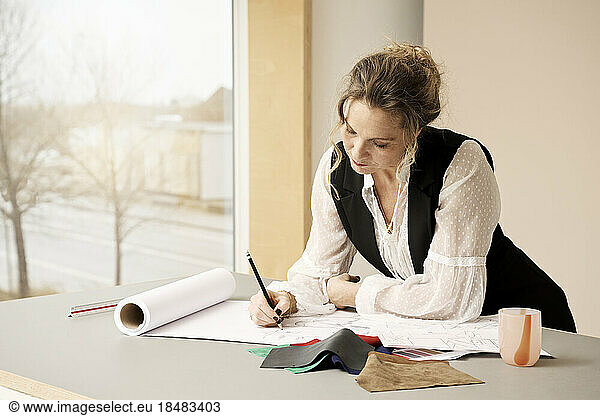 Mature fashion designer sketching on paper in studio